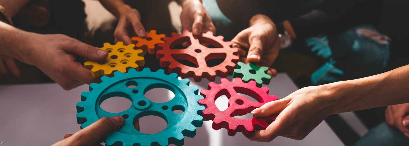 Menschen, die Zahnräder halten, als Sinnbild für das Miteinander