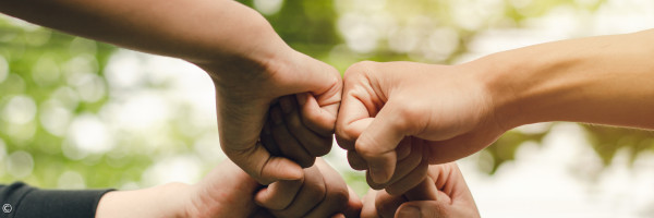 Vier aneinander gehaltene Fäuste für die Zusammenarbeit im Leitenden Kreis